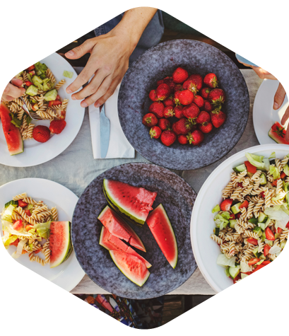 Overhead view of plates with salad, pasta, strawberries, and watermelon on a table.