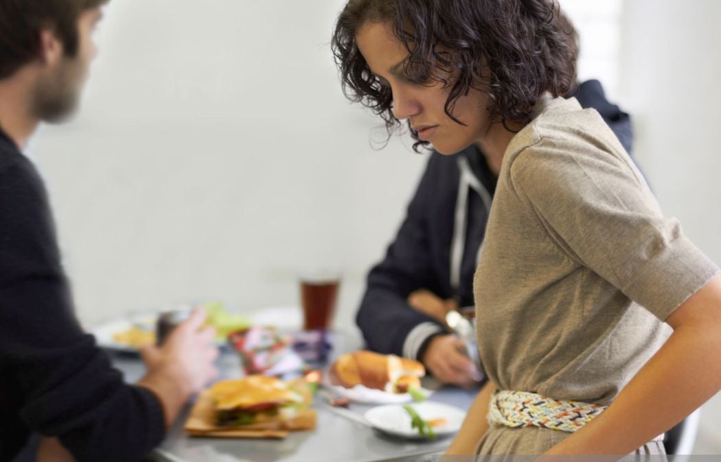 Person sitting at a table looking away from food while others eat.