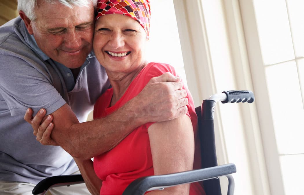 Person in a wheelchair being hugged by another person indoors.