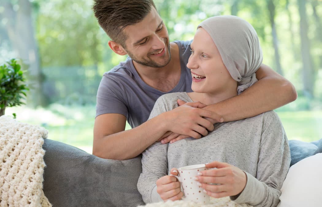 Person embracing and comforting another person wearing a headscarf on a couch.