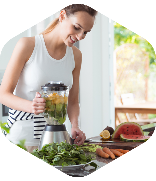 Person using a blender with fruits and vegetables in a bright kitchen.