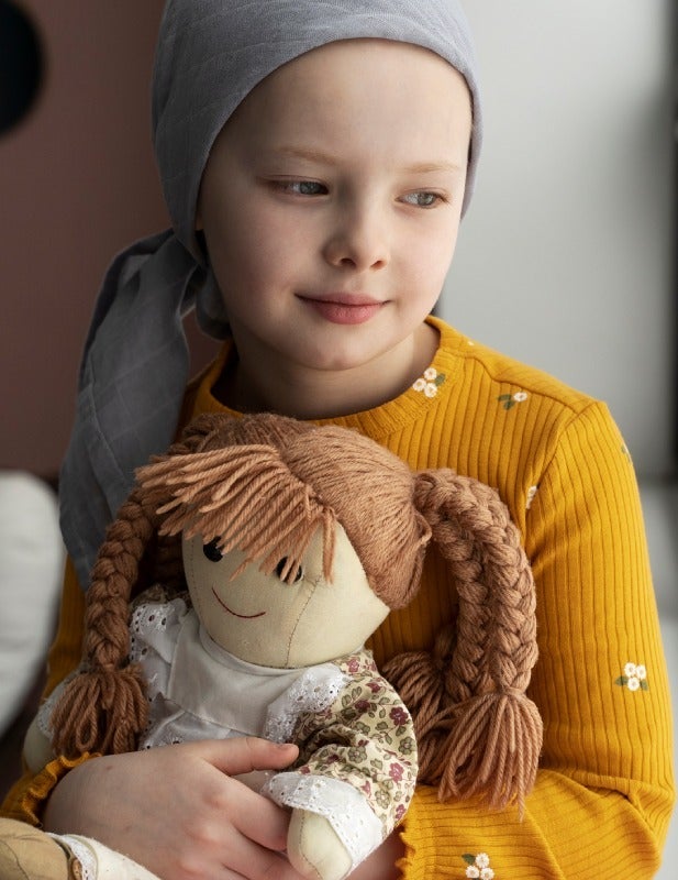 Child wearing a headscarf holding a soft doll indoors.