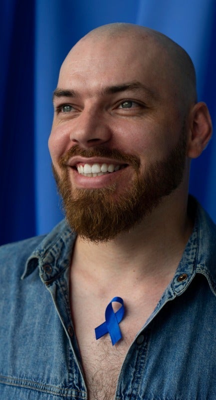 Person with a beard wearing a blue awareness ribbon on a shirt.